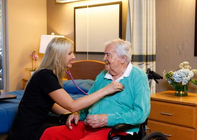nursing aide using a stethoscope to an elderly man on a wheelchair
