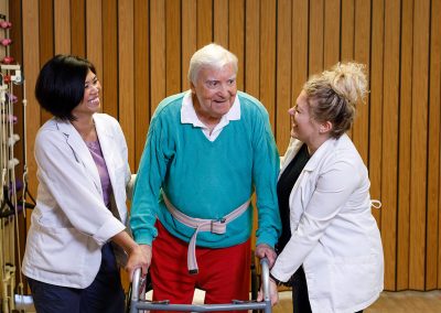 two healthcare aides doing therapy on an elderly man